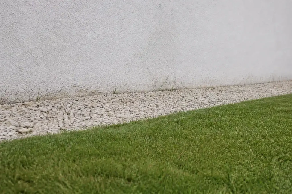 Gravier clair au pied du mur blanc, herbe tondue