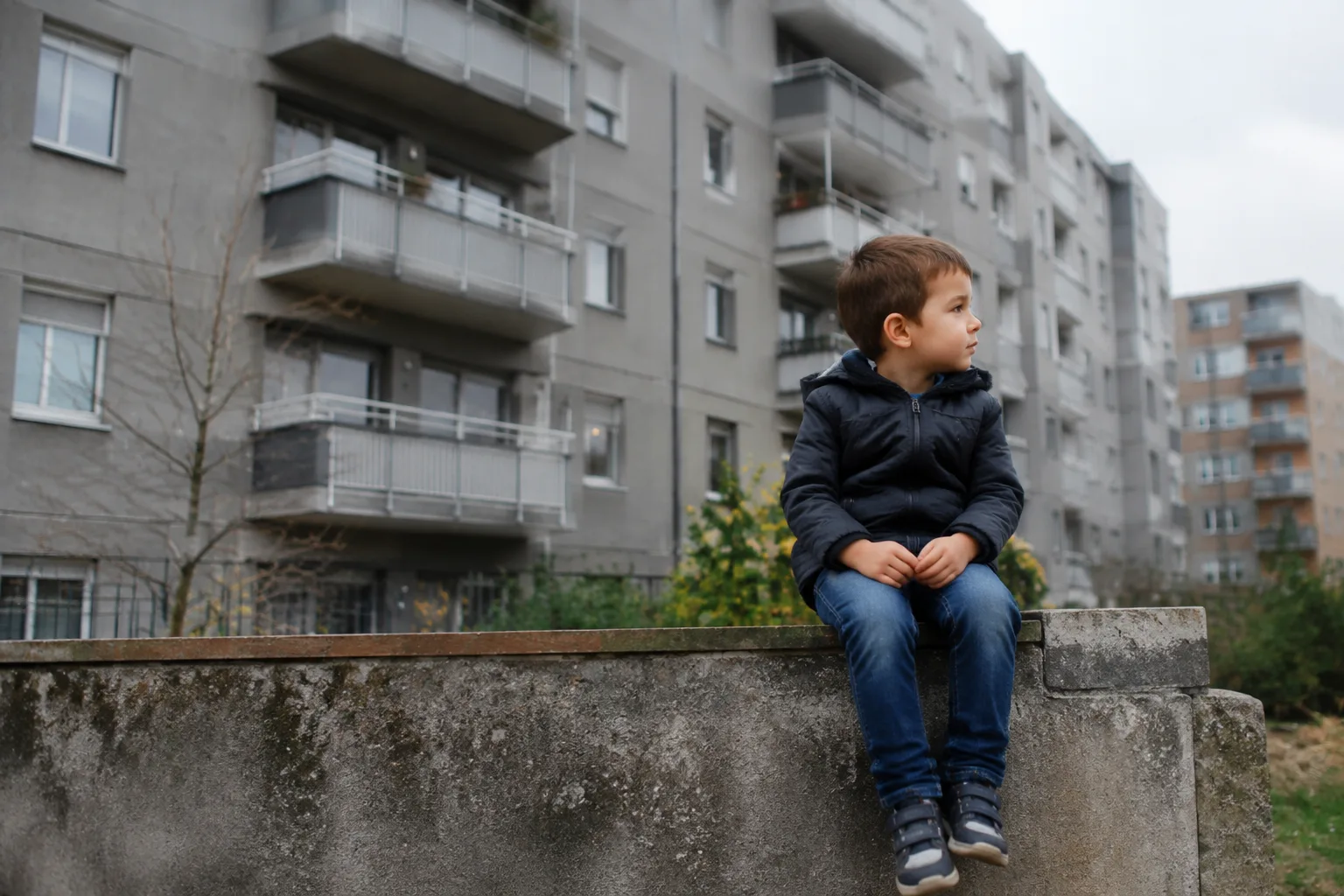 Immeubles gris avec balcons, un enfant assis sur muret
