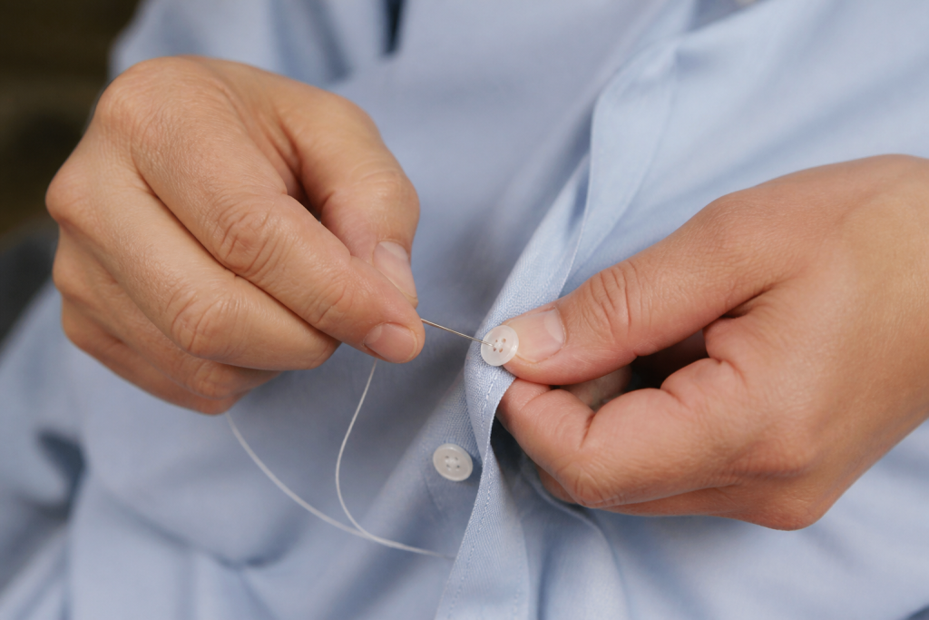 Mains recousant un bouton sur une chemise bleue claire